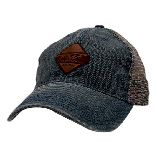A blue denim baseball cap with a leather tidewater patch on the front and a grey mesh back.